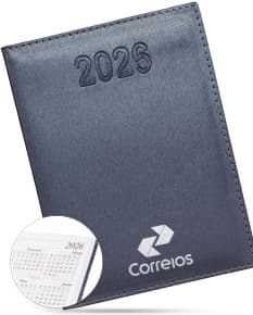 Agenda Diária 2025 de capa preta com detalhes dourados e páginas em branco, sobre uma mesa de madeira com caneta ao lado.