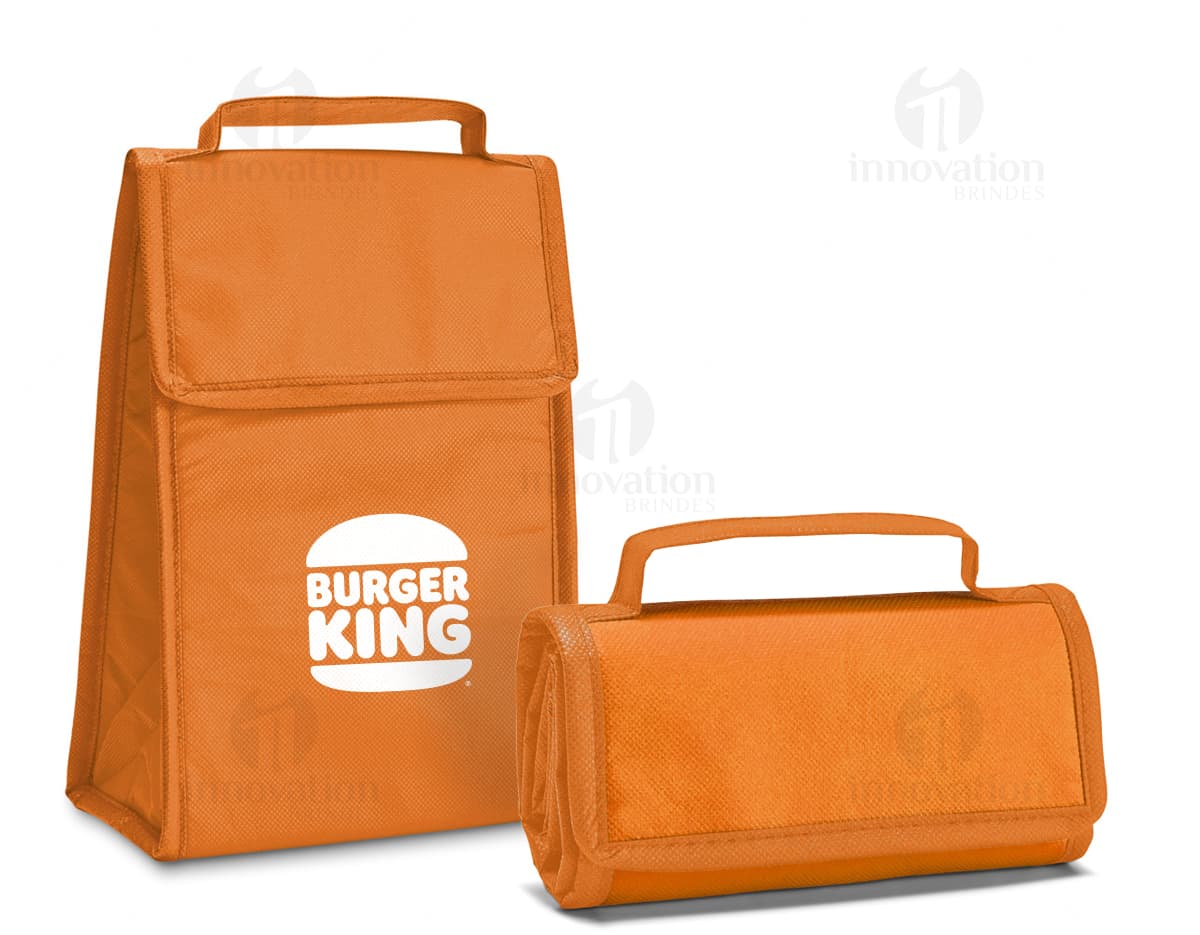 Bolsa térmica dobrável em formato 3D, vazia e aberta, com design moderno e clean. Está sobre uma mesa ao lado de um computador, um notebook e um dispenser de sabonete. A imagem contém elementos como embalagem de plástico, papel em branco, ícones de tecnologia e etiquetas de informação.