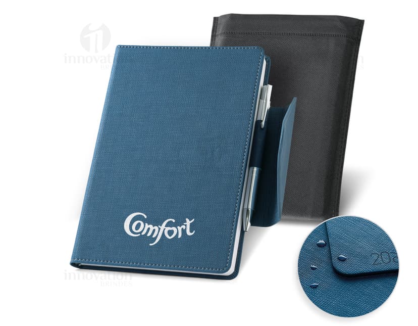 Agenda A5 preta com fecho magnético e suporte, sobre um notebook preto. Na imagem também há um livro, papel em branco, teclado e chave. Queremos trazer riqueza, organização e sucesso para seu escritório.