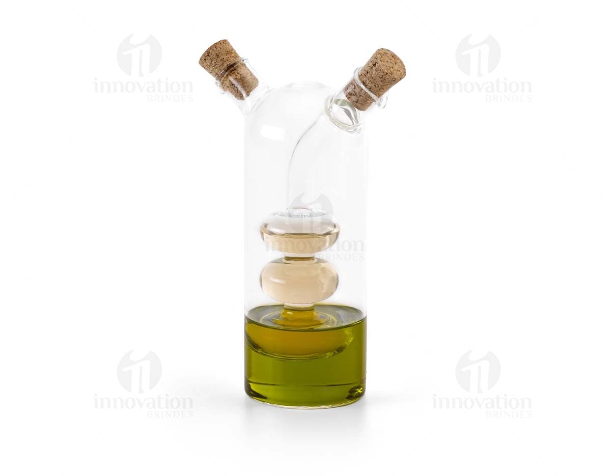 Galheteiro de vidro com três recipientes, um para azeite, outro para vinagre e um terceiro para molho de pimenta. Cada recipiente possui uma tampa de metal e um bico dosador. O galheteiro está sobre uma mesa de madeira escura.
