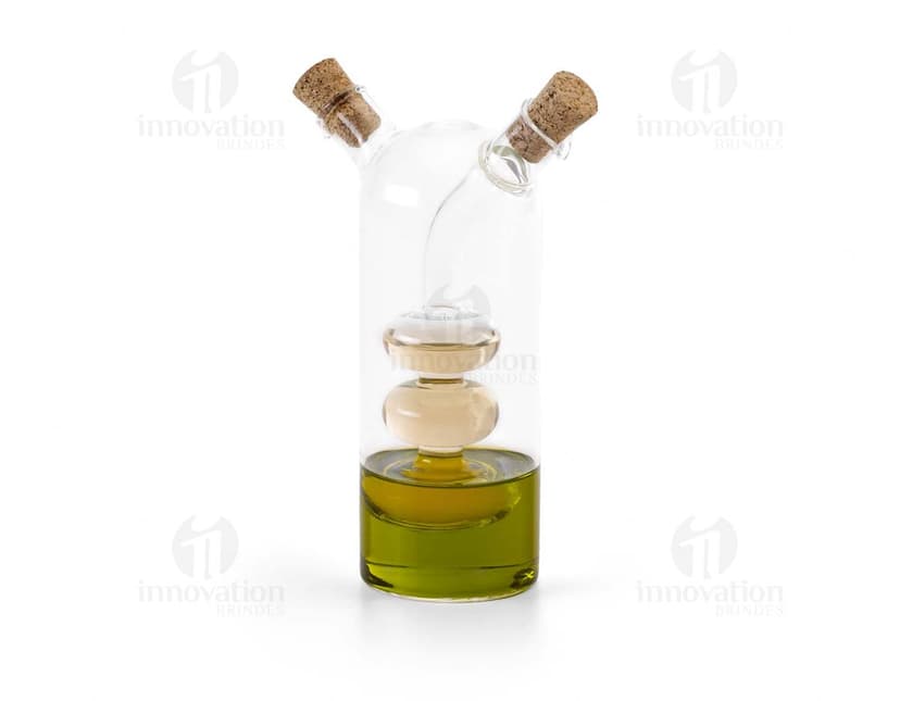 Galheteiro de vidro com três recipientes, um para azeite, outro para vinagre e um terceiro para molho de pimenta. Cada recipiente possui uma tampa de metal e um bico dosador. O galheteiro está sobre uma mesa de madeira escura.