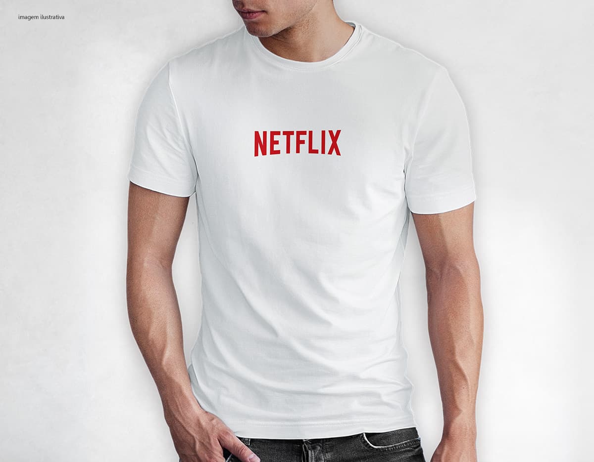 Homem jovem e atraente sorrindo, posando em um estúdio com uma camiseta preta de algodão tradicional de 165g/m². Ele está vestindo jeans, tem cabelo escuro e expressão feliz. O modelo está em pé, com um sorriso confiante, e possui uma aparência moderna e masculina.