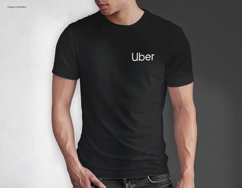 Homem jovem e atraente sorrindo, posando em um estúdio com uma camiseta preta de algodão tradicional de 165g/m². Ele está vestindo jeans, tem cabelo escuro e expressão feliz. O modelo está em pé, com um sorriso confiante, e possui uma aparência moderna e masculina.