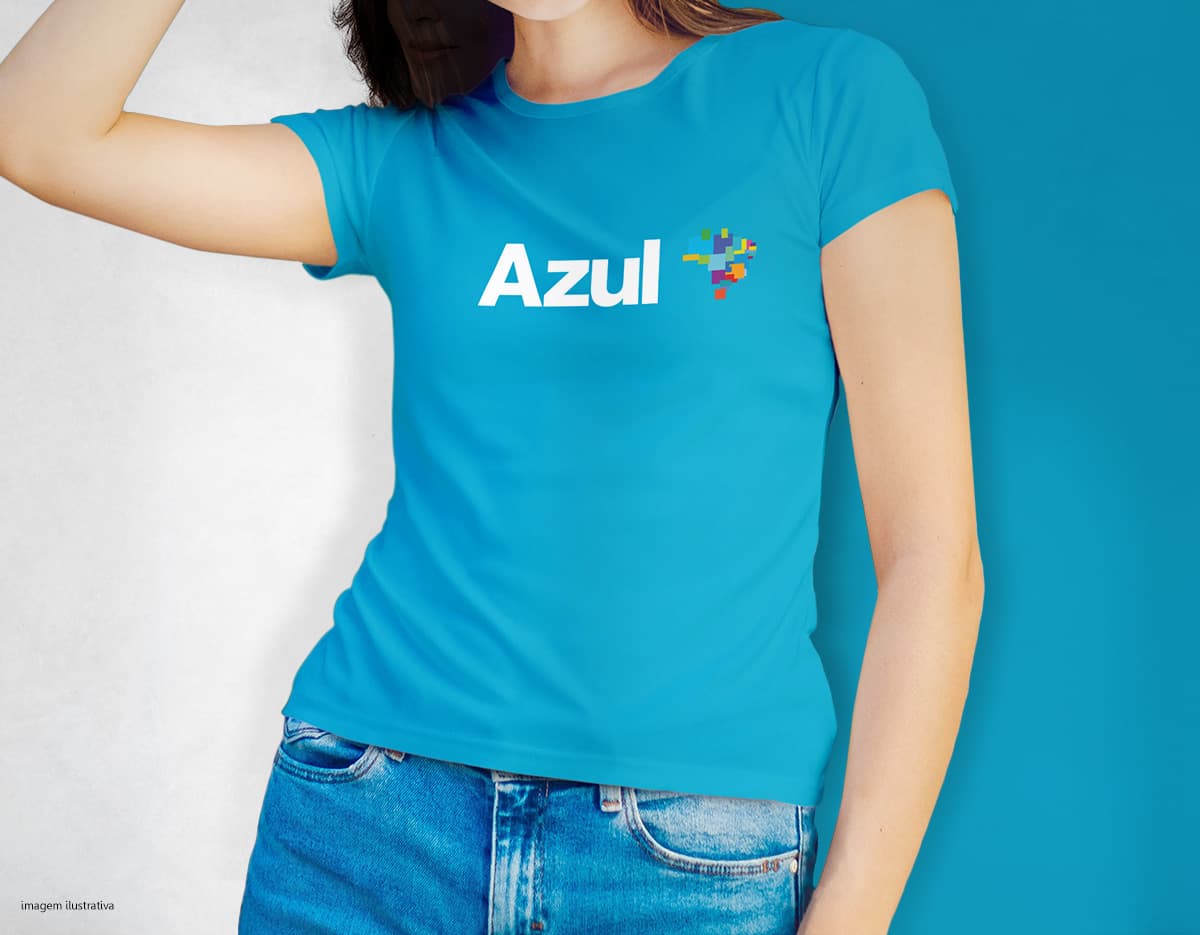 Camiseta feminina de corte cinturado em cor azul, usada por uma modelo sorridente e atraente. Ela está posando de forma casual e elegante, com cabelo escuro e jeans. A roupa é moderna e estilosa, perfeita para mulheres jovens e modernas.