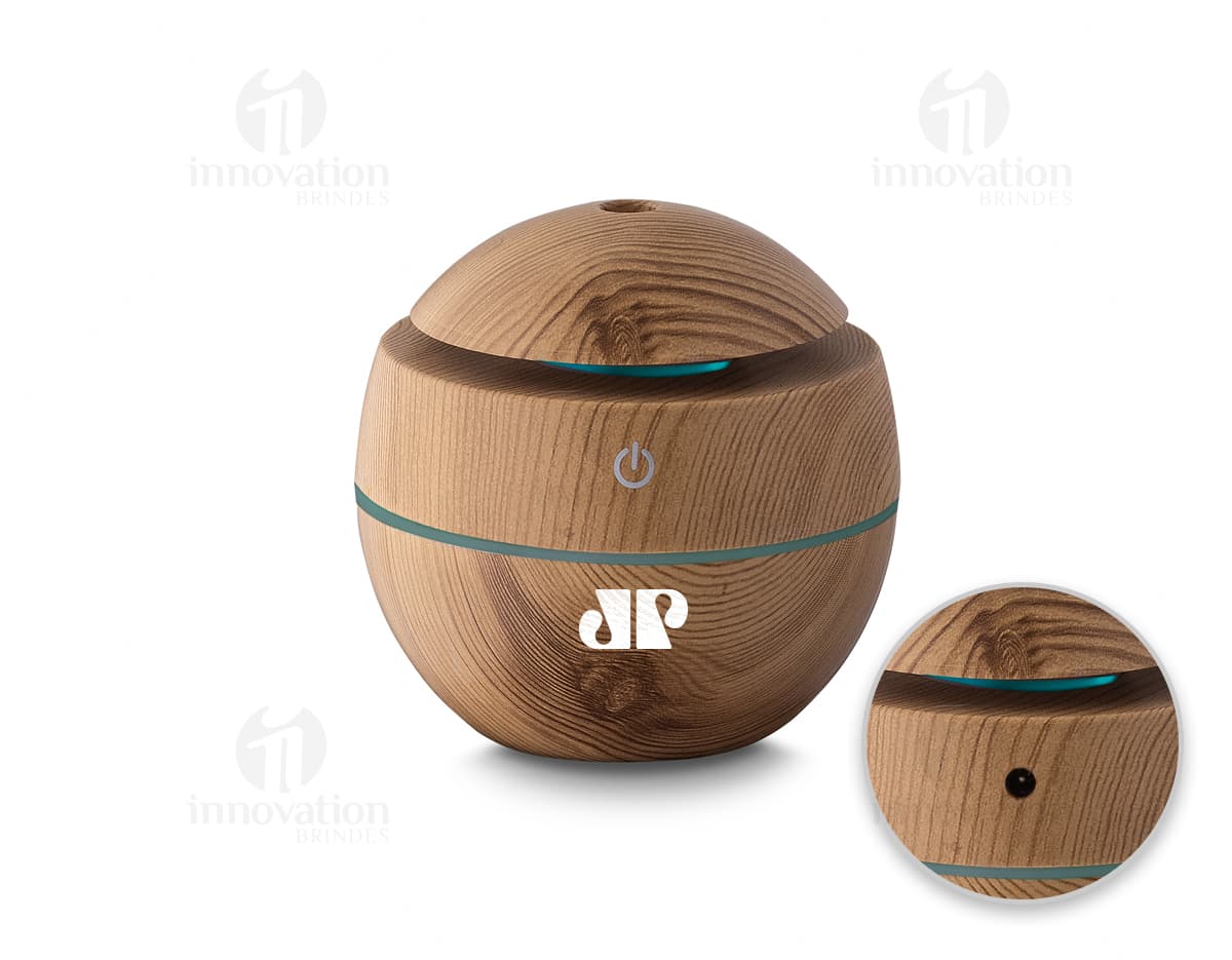 Umidificador de ar USB em ABS reciclável, que aparece em uma cesta de vime marrom ao lado de um banco, comida, dinheiro e outros objetos. A imagem é de vista próxima, com foco no produto e nos detalhes dos materiais utilizados.