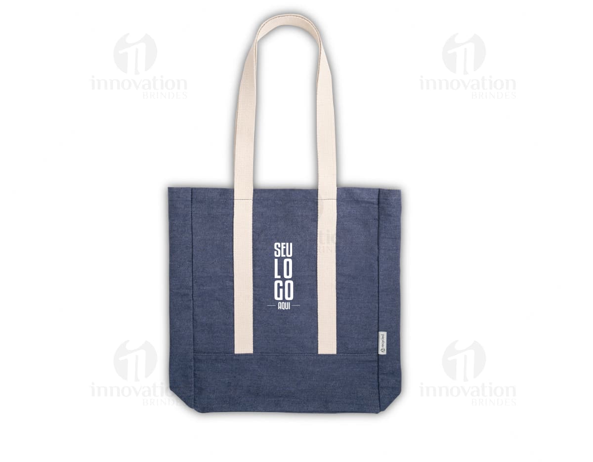 Sacola de denim reciclado com bolso, em tons de marrom e amarelo. Possui alça em couro, fecho com cadeado e etiqueta de preço. Ideal para compras e presente, demonstrando elegância e versatilidade.