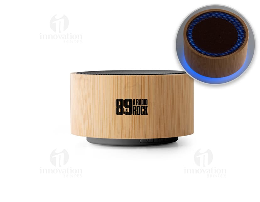 : Caixa de som de bambu e ABS com Bluetooth versão 5.0 em close-up, sobre um bloco de corte. O objeto é metálico, de cor marrom e possui empilhados muffins e cupcakes, com cobertura de chocolate e creme. O dispositivo é brilhante e reflete a luz, indicando alta qualidade.