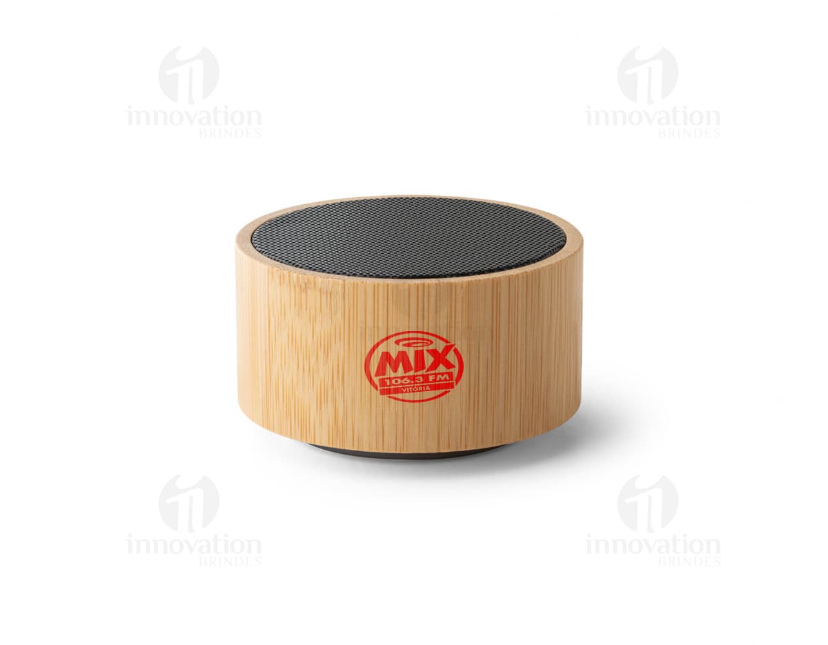 : Caixa de som de bambu e ABS com Bluetooth versão 5.0 em close-up, sobre um bloco de corte. O objeto é metálico, de cor marrom e possui empilhados muffins e cupcakes, com cobertura de chocolate e creme. O dispositivo é brilhante e reflete a luz, indicando alta qualidade.