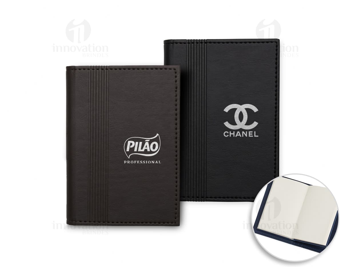 Bloco de anotações com porta caneta em um escritório vazio. O caderno está aberto em uma página em branco e ao lado há um videodisco. O design é moderno e conta com um espaço para guardar objetos, como canetas. O ambiente é limpo e organizado, com um ar de nostalgia.