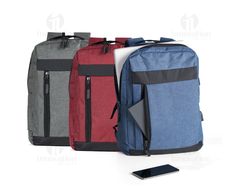 Homem de negócios usando um dispositivo eletrônico em um avião, com uma mochila de nylon preta nas costas. O bolso da mochila contém um cabo USB e há um jeans preto amarrado ao redor da alça.