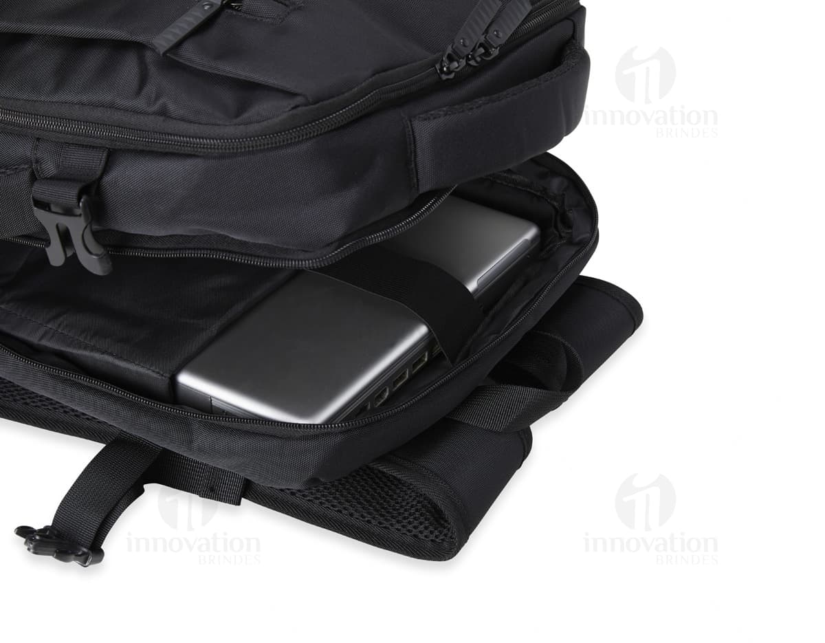 Homem de negócios usando um elegante terno preto, segurando uma mochila de nylon preta de 20 litros com USB. O acessório tem apoio nas costas, alça, e suporte para objetos.