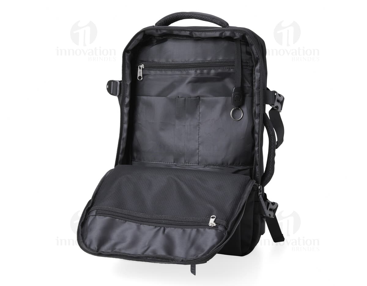 Homem de negócios usando um elegante terno preto, segurando uma mochila de nylon preta de 20 litros com USB. O acessório tem apoio nas costas, alça, e suporte para objetos.