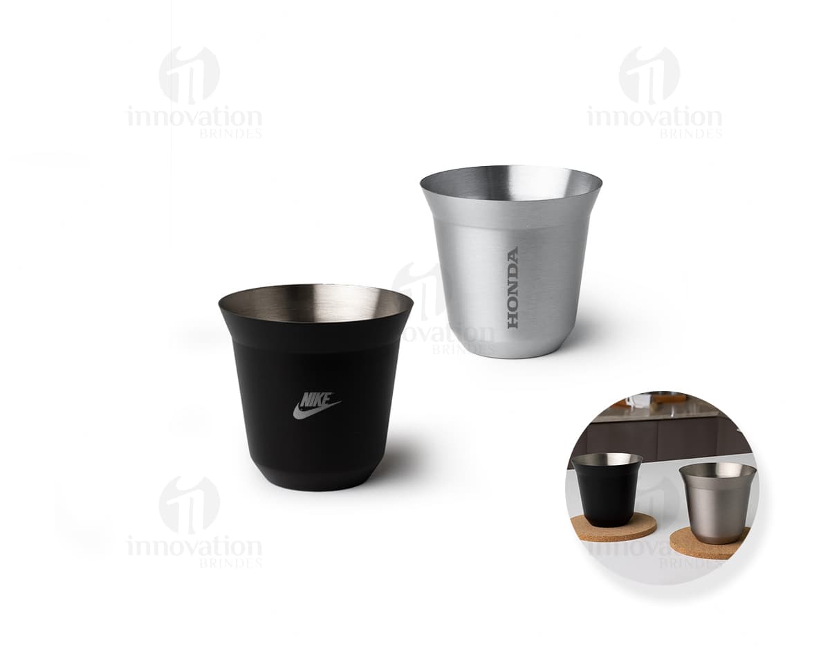 Copo de Inox de 100ml em uma mesa, ao lado de uma xícara de chá e diversos utensílios de cozinha. O copo está vazio, limpo e brilhante, com um design elegante.