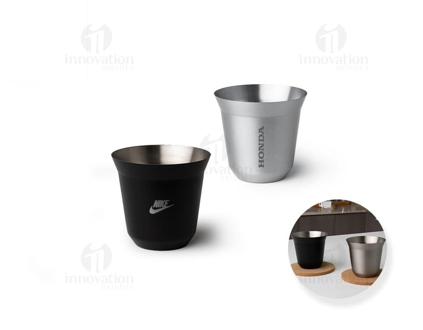 Copo de Inox de 100ml em uma mesa, ao lado de uma xícara de chá e diversos utensílios de cozinha. O copo está vazio, limpo e brilhante, com um design elegante.