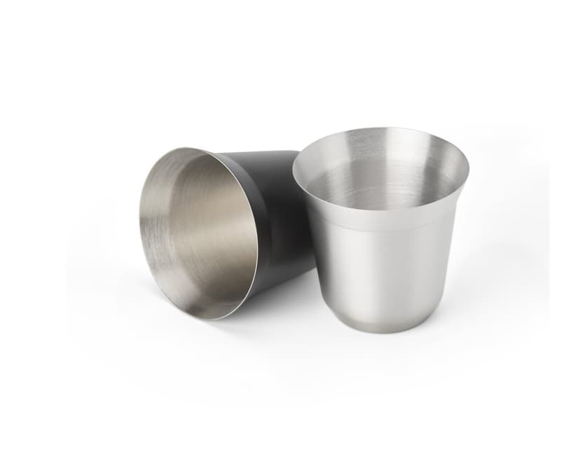 Copo de Inox de 100ml em uma mesa, ao lado de uma xícara de chá e diversos utensílios de cozinha. O copo está vazio, limpo e brilhante, com um design elegante.
