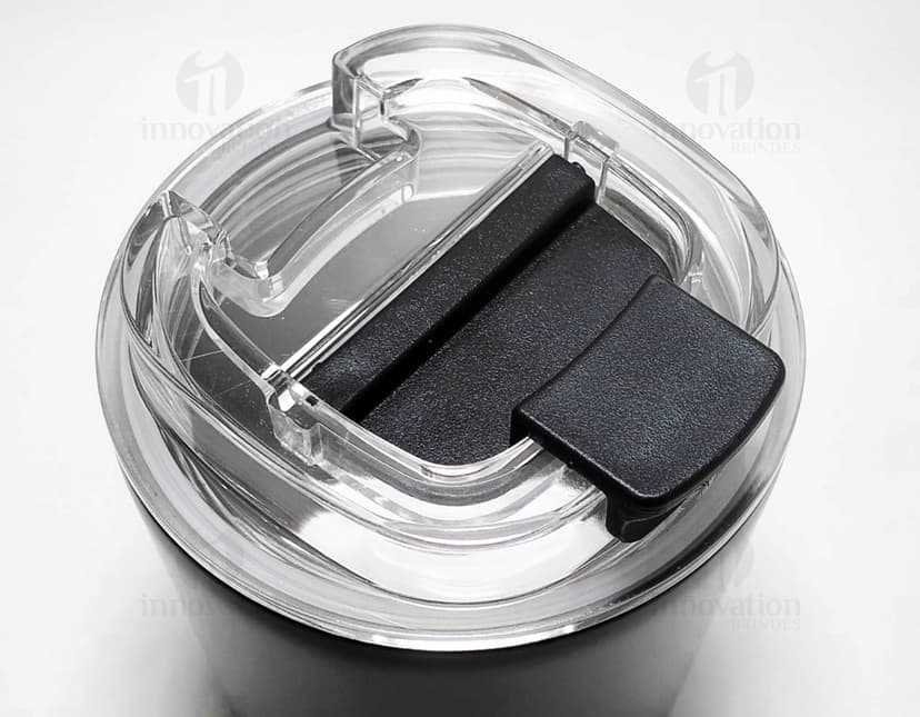Copo térmico de 280ml em cerâmica preta e metal de cor prateada, com alça e tampa. O copo está vazio e posicionado sobre uma mesa de cozinha, ao lado de uma colher, uma jarra de café e alguns utensílios.
