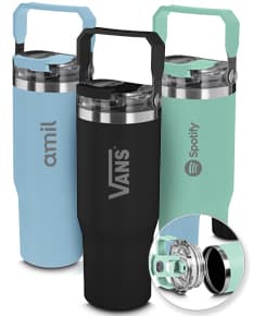 Garrafa térmica de cor vermelha com tampa de rosquear e alça para transporte. A garrafa está sobre uma mesa de madeira e ao fundo é possível ver uma xícara de café e um vaso de flores.