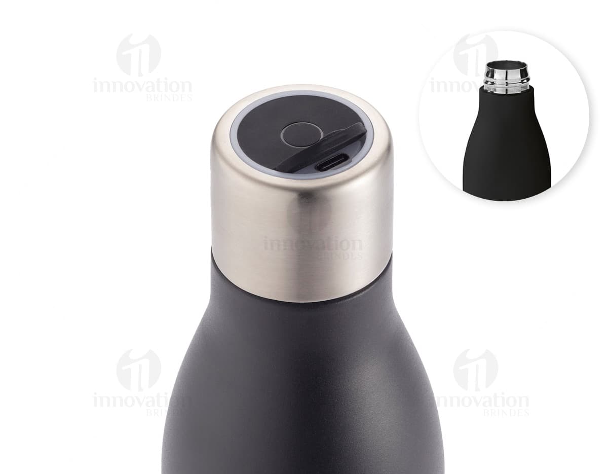 Garrafa em aço inox contendo bebida alcoólica, com tampa de cortiça. A garrafa está vazia e possui rótulo em branco. Está em pé sobre uma superfície de vidro, com reflexo no fundo escuro. A imagem é vertical e destaca a elegância e luxo do produto.