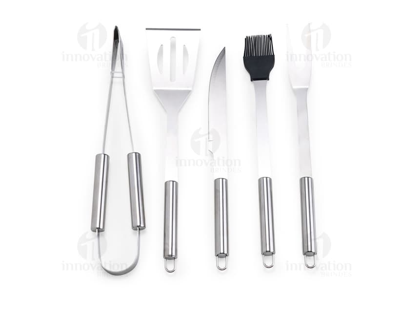 Kit Churrasco 5 Peças - Conjunto contendo faca, garfo, pinça, espátula e escova para churrasco em fundo de madeira.