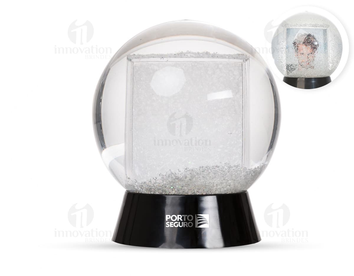 Globo de neve plástico transparente com uma paisagem de neve e uma pequena figura de um boneco de neve no centro.