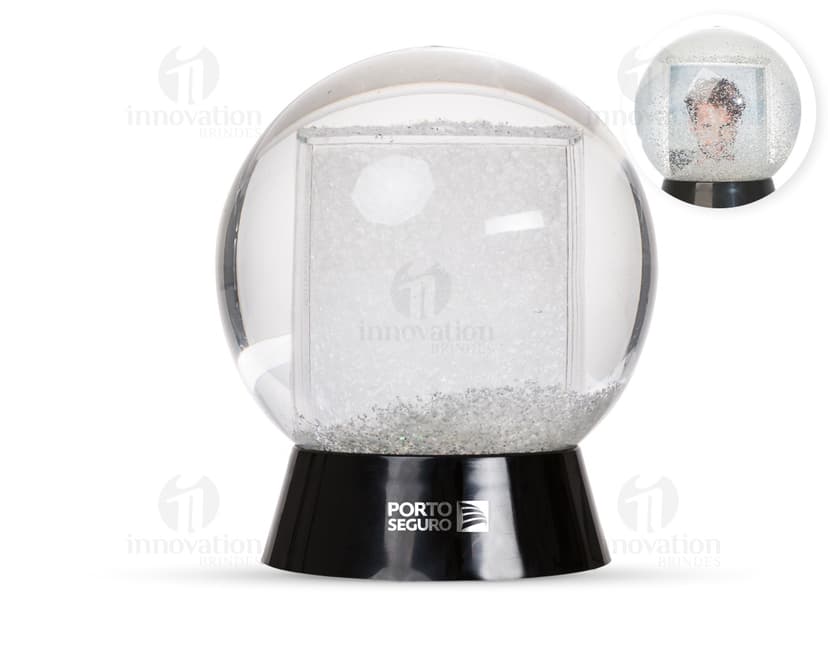 Globo de neve plástico transparente com uma paisagem de neve e uma pequena figura de um boneco de neve no centro.