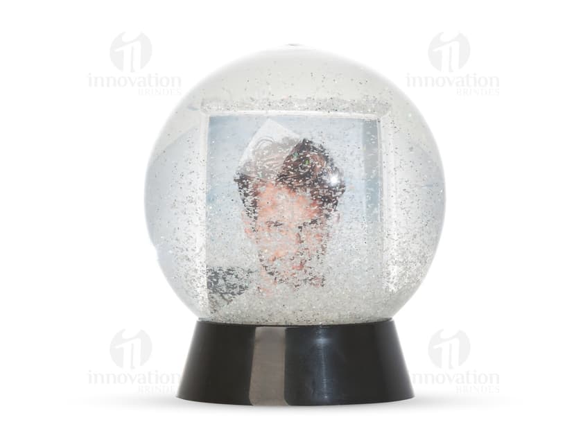 Globo de neve plástico transparente com uma paisagem de neve e uma pequena figura de um boneco de neve no centro.